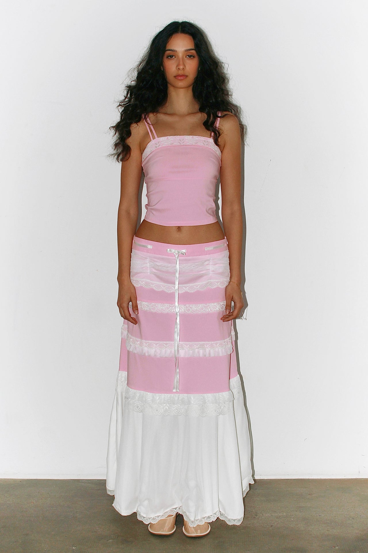 Front view of a woman wearing a pink and white outfit – pink bandeau top with a long white skirt featuring pink bands, elegant summer silhouette.