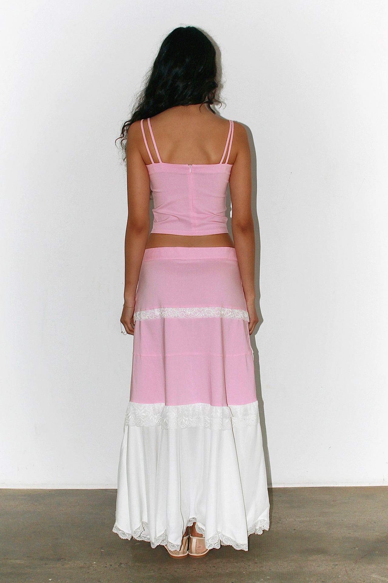 Front view of a woman wearing a pink and white outfit – pink bandeau top with a long white skirt featuring pink bands, elegant summer silhouette.