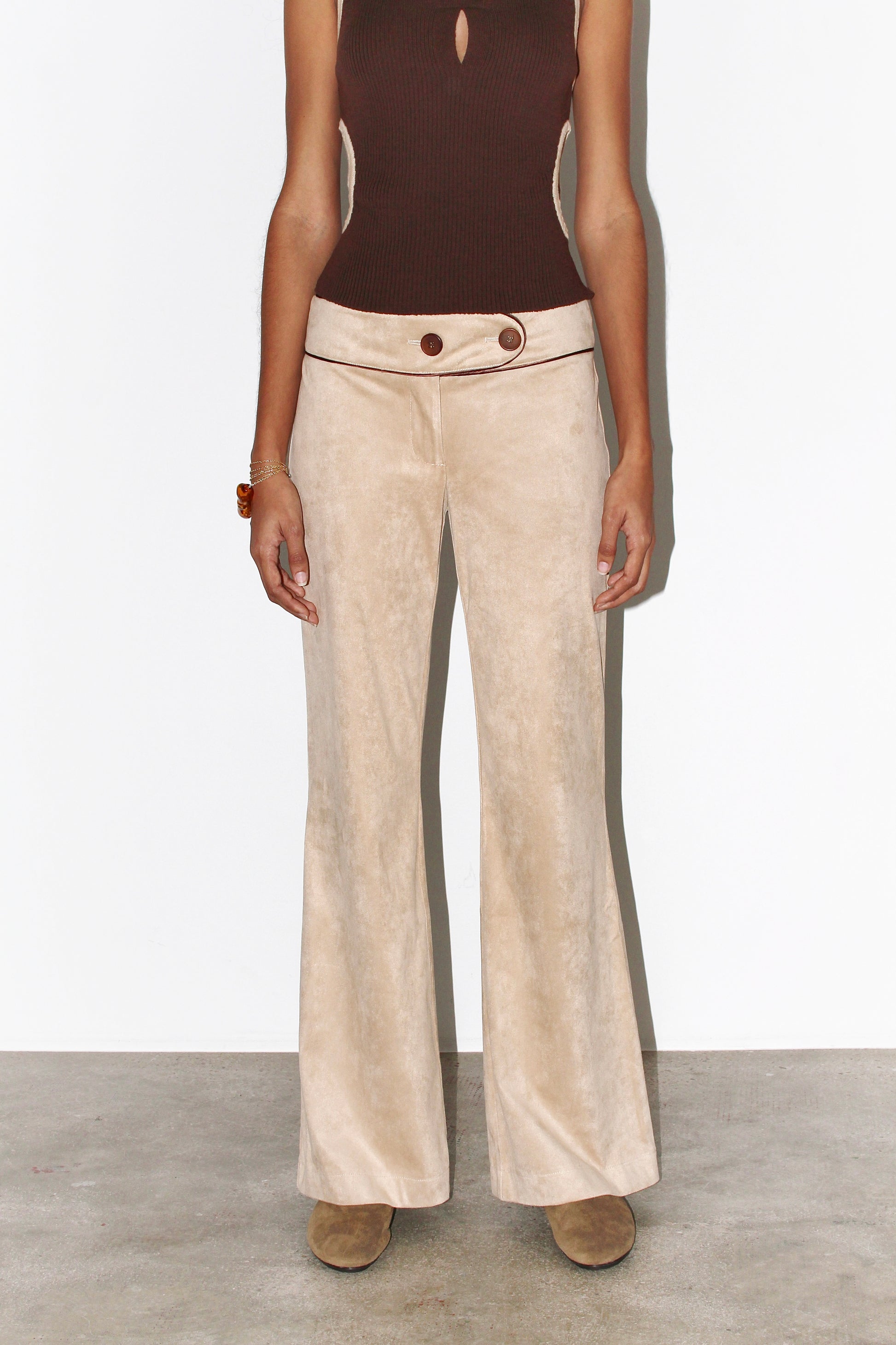 Front view of the Andrea Pants in beige suede with contrasting brown piping, featuring a low-rise fit, curved waistband, and signature front button detail.