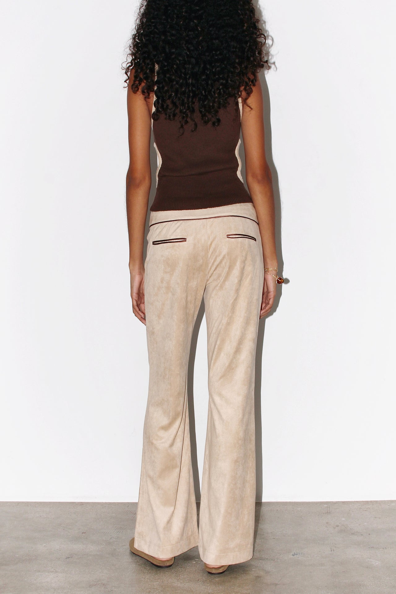 Front view of the Andrea Pants in beige suede with contrasting brown piping, featuring a low-rise fit, curved waistband, and signature front button detail.