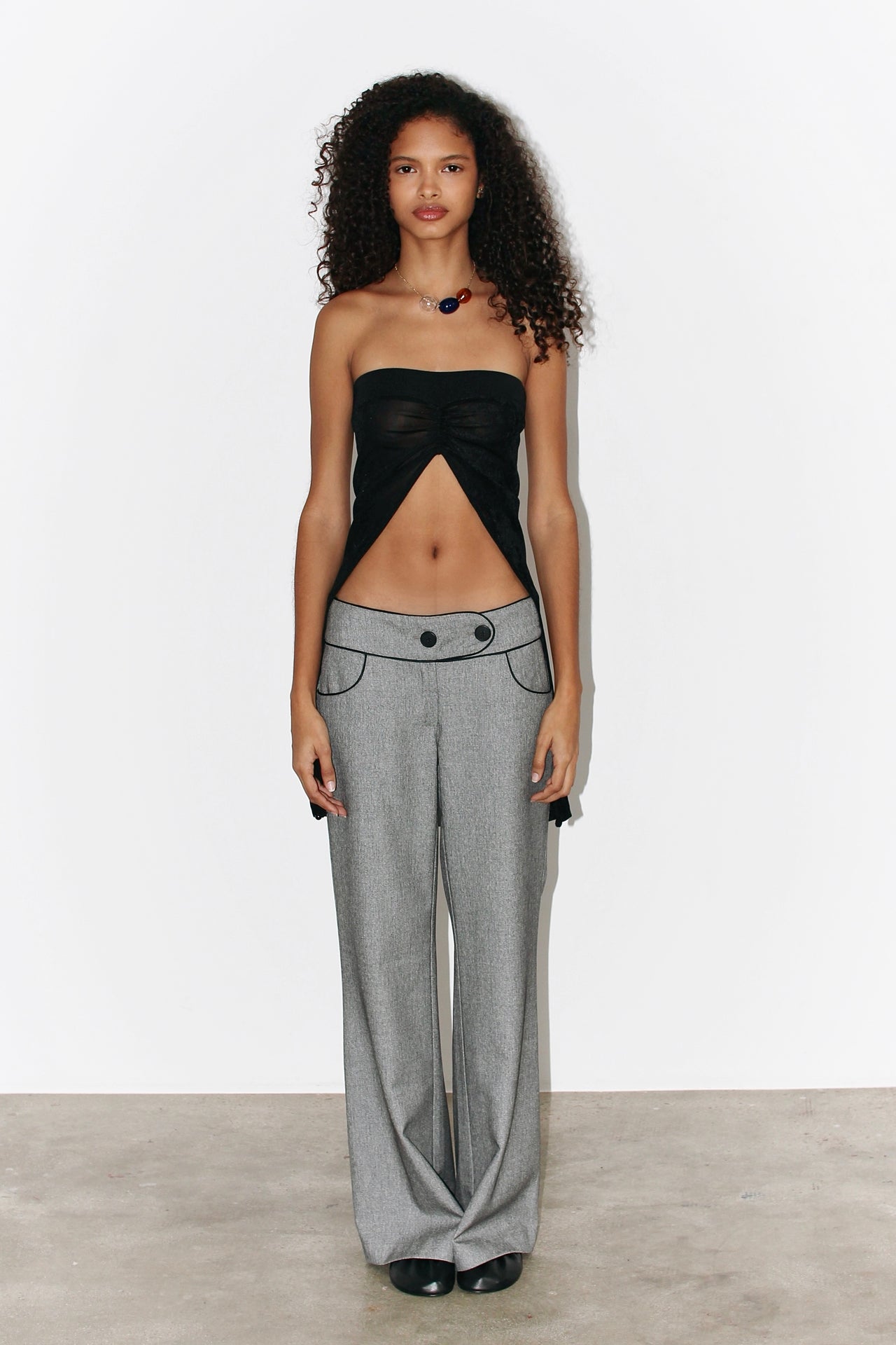 Front view of the Andrea Pants in soft grey with contrasting black piping, showcasing the low-rise fit and curved waistband.