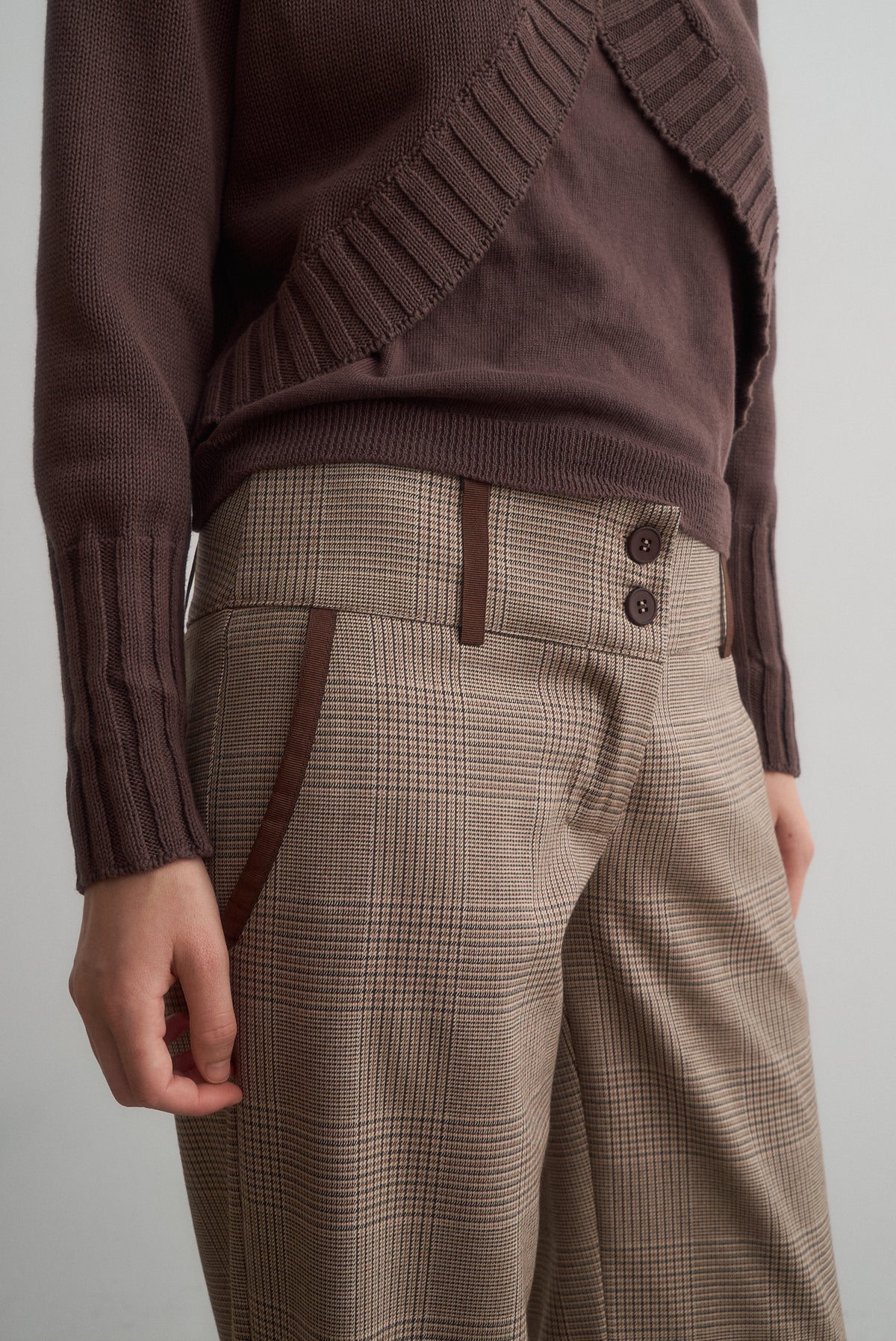 Close-up of Carlita brown cardigan and top above Lavinia checked trousers with double-button closure.