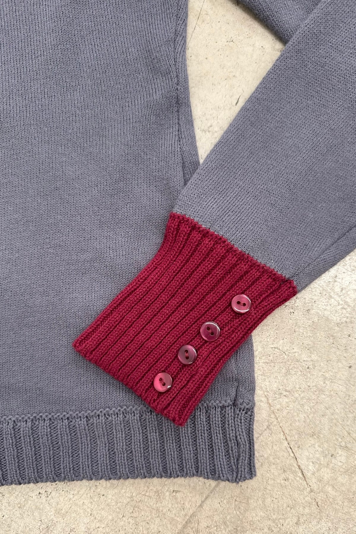 Close-up of the Ines grey knit top with burgundy ribbed cuffs and button detailing.