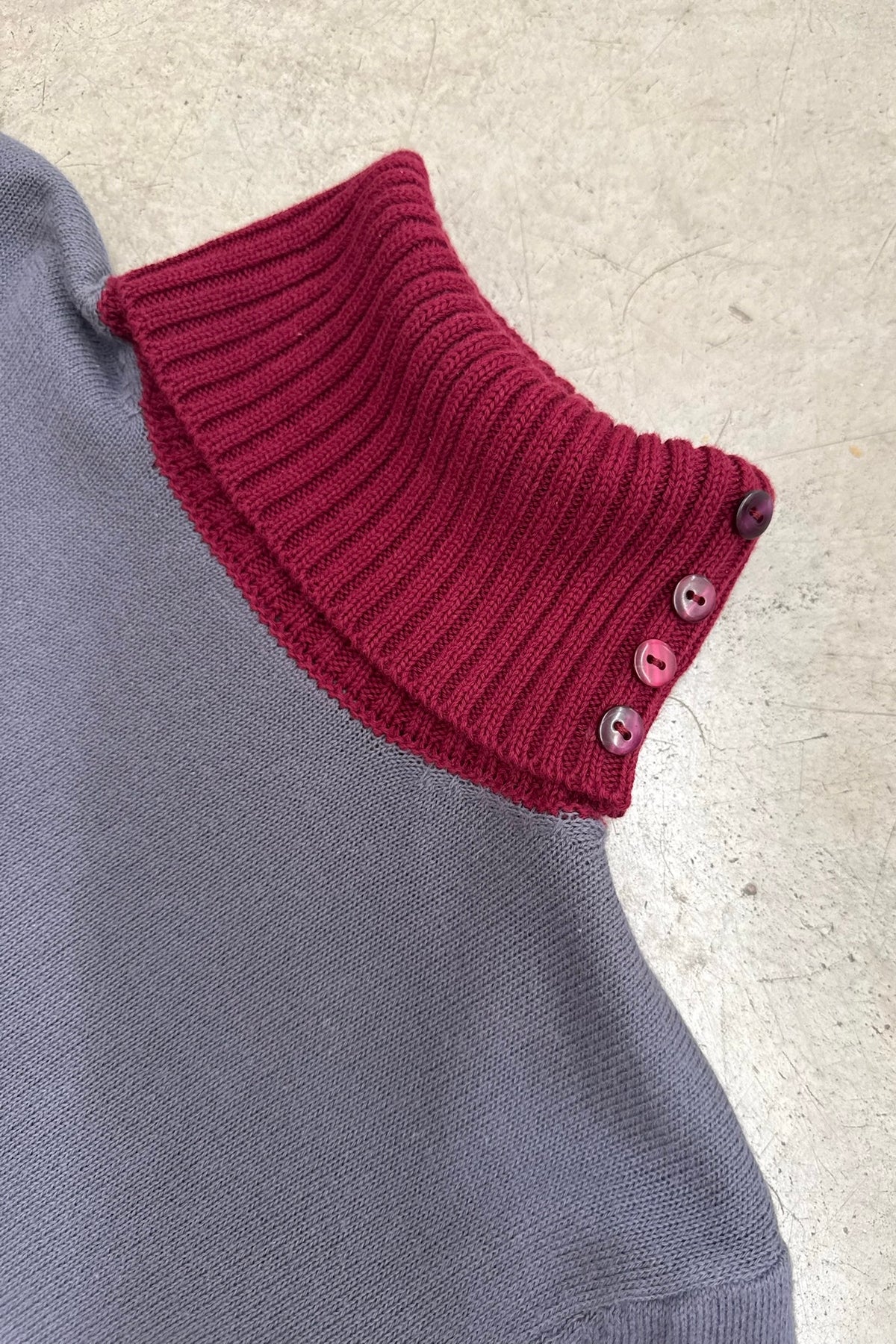 Close-up of the Ines grey knit top with a burgundy ribbed roll neck and side buttons.