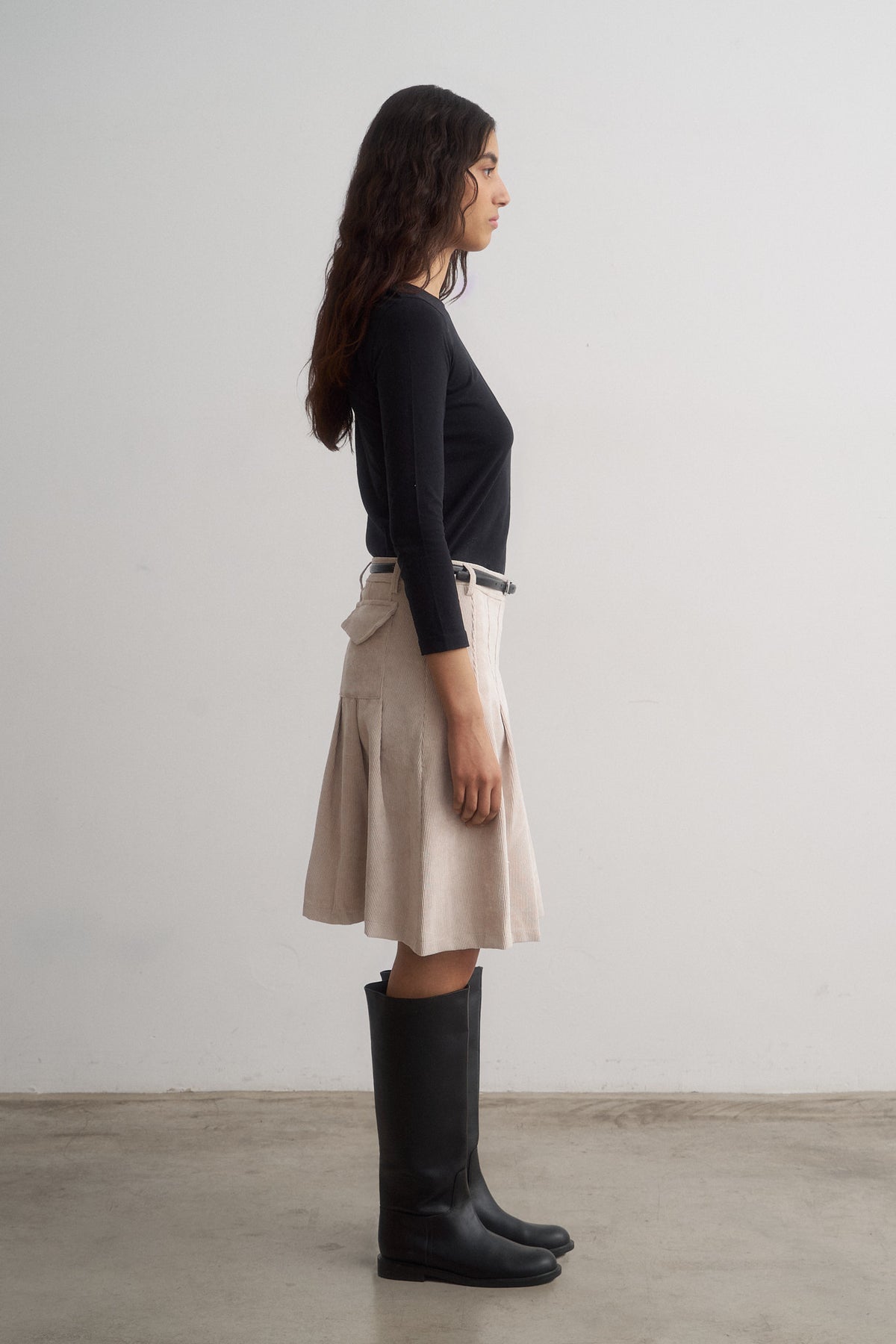 Evie ivory pleated skirt worn with a black top and boots, side view