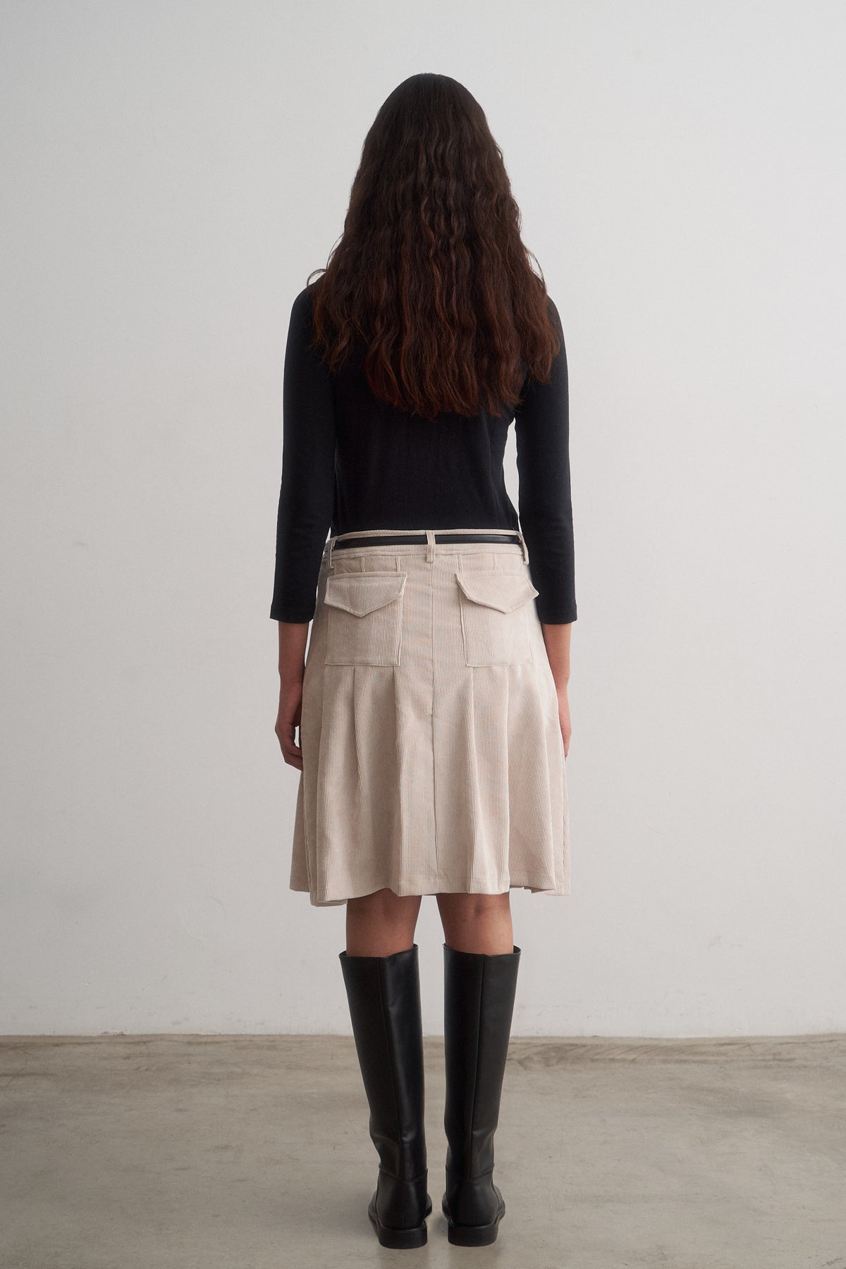 Evie ivory pleated skirt worn with a black top and boots, rear view