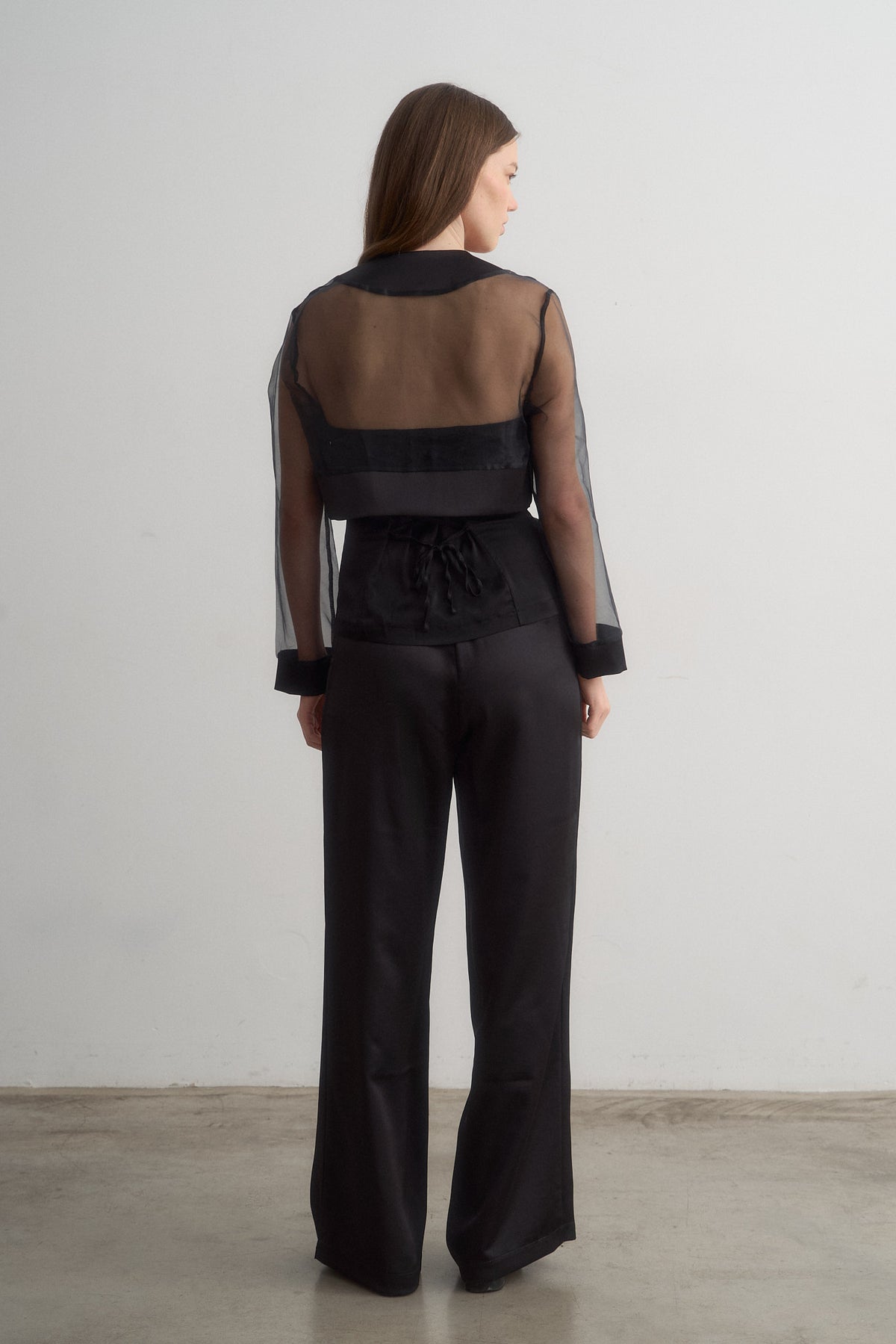 Lavi black wide-leg trousers worn with a sheer jacket, full-length rear view