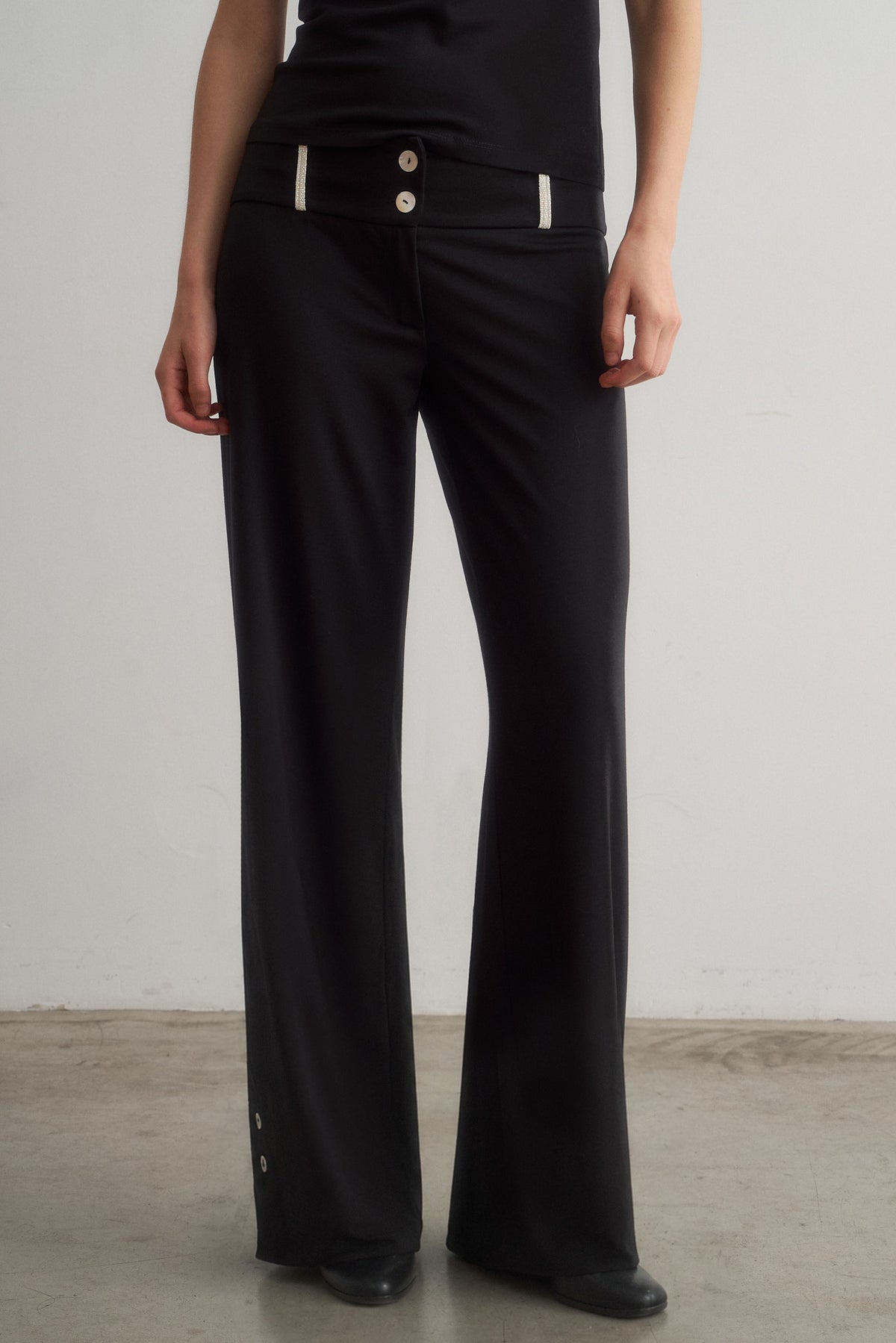 Zeynep black wide-leg trousers, front detail showing waistband trim and buttons